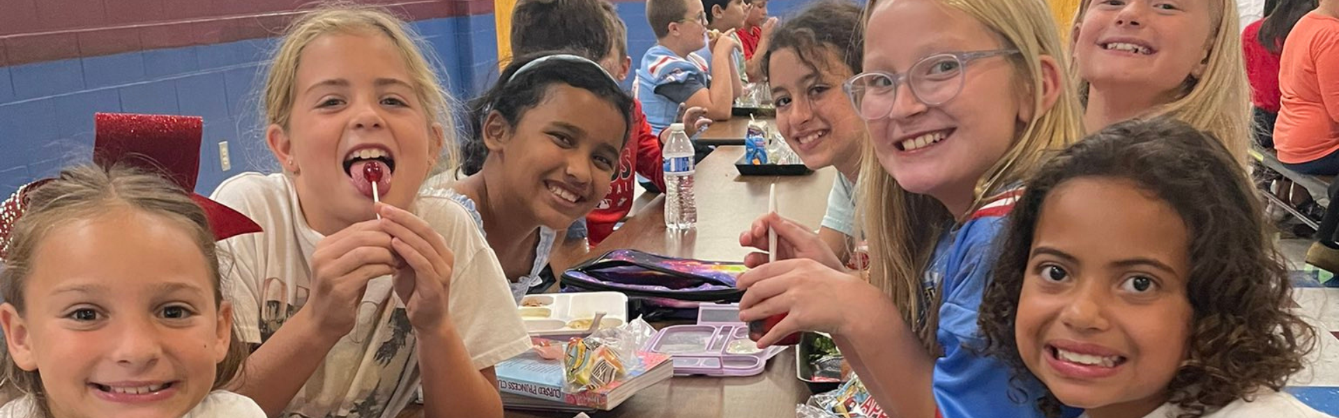 seven young girls sitting at the lunch table smiling for a picture